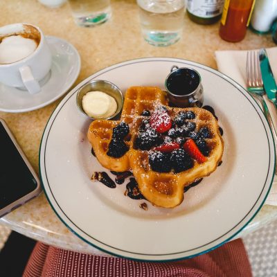A cup of coffee next to a plate with a waffle shaped like Texas topped with berries and sugar.